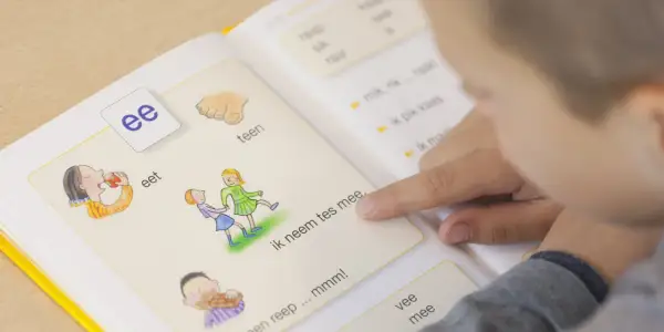 Kind leert woordenschat groep 3 uit een boekje. De letter 'ee' staat centraal, met illustraties van eten en spelen.