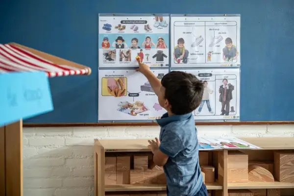 Jongen wijst naar een poster met kledingstukken en geld, onderdeel van woordenschat groep 4.