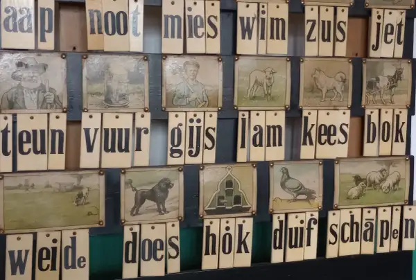 Oude letterkaarten met afbeeldingen, die samen Nederlandse uitdrukkingen vormen zoals 'aap, noot, mies'.