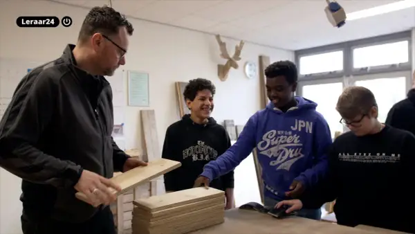 Docent toont hout aan leerlingen. Een van hen, met een blauwe hoodie, lacht. Dit is een cluster 4 indicatie voor praktijkonderwijs.