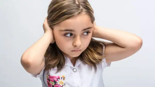 Meisje met handen op de oren, probeert overprikkeling te voorkomen. Ze kijkt weg, alsof ze de wereld even buiten wil sluiten.