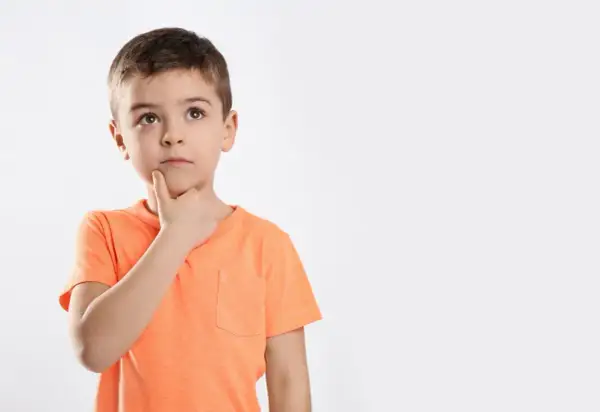 Jongetje met oranje shirt denkt diep na, misschien een beetje traag van begrip, met zijn vinger op zijn kin.