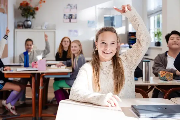 Vrolijke leerlingen steken hun hand op in een klaslokaal. De sfeer is positief, ondanks de mogelijke particulier onderwijs kosten.