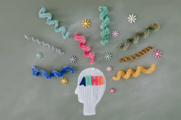 Kleurrijke linten en bloemen omringen een hoofdprofiel met de letters "ADHD". Dit symboliseert de zoektocht naar een kind behandeling.