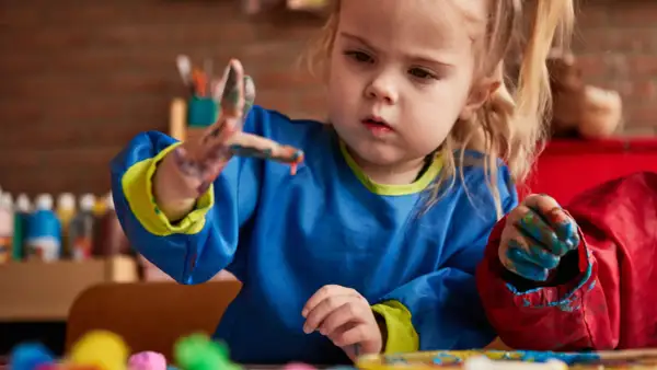 Een peuter met verf aan haar handen, die geconcentreerd aan het schilderen is. Dit is een mooi voorbeeld van cognitieve ontwikkeling peuter door creatief spel.
